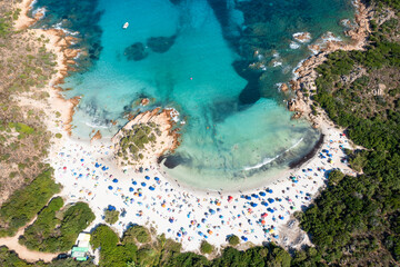 View from above, stunning aerial view of a white sand beach full of beach umbrellas and people swimming in a turquoise water. Spiaggia del Principe, Costa Smeralda, Sardinia, Italy.