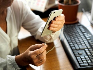 Female hands connect the charger to a smartphone at a work desk.