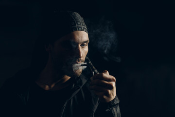 Man smokes smoking pipe against dark background. Back side lit profile portrait with smoke