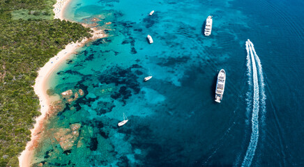 View from above, stunning aerial view of a green coastline with a white sand beach and and boats sailing on a turquoise water at sunset. Cala di volpe beach,Sardinia, Italy.