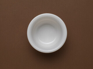 An empty deep white bowl on a brown background.