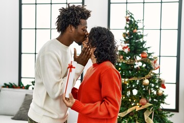 Young interracial couple smiling happy and hugging holding christmas gift at home.
