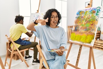 Obraz premium Young hispanic woman at art studio pointing fingers to camera with happy and funny face. good energy and vibes.