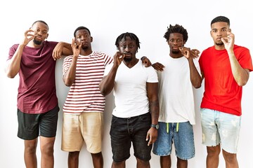 Young african group of friends standing together over isolated background mouth and lips shut as zip with fingers. secret and silent, taboo talking