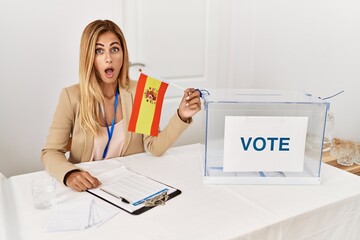 Blonde beautiful young woman at political campaign election holding spain flag scared and amazed with open mouth for surprise, disbelief face