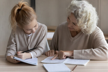 Loving mature Caucasian grandmother help little teen granddaughter with school homework assignment....