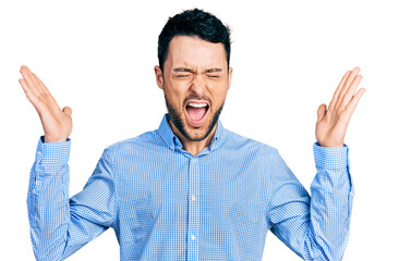 Fototapeta premium Hispanic man with beard wearing casual business shirt celebrating mad and crazy for success with arms raised and closed eyes screaming excited. winner concept