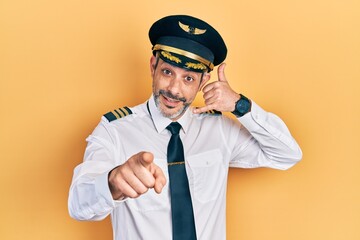 Handsome middle age man with grey hair wearing airplane pilot uniform smiling doing talking on the telephone gesture and pointing to you. call me.