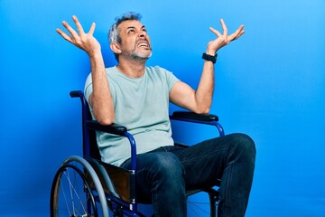 Handsome middle age man with grey hair sitting on wheelchair crazy and mad shouting and yelling...