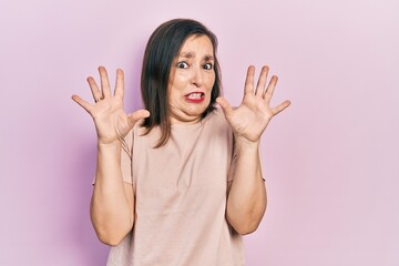Middle age hispanic woman wearing casual clothes afraid and terrified with fear expression stop gesture with hands, shouting in shock. panic concept.