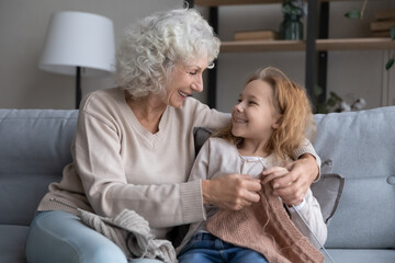 Loving happy mature Caucasian grandmother teach small teen granddaughter knit with needles. Smiling...