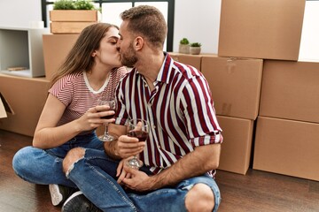 Young caucasian couple toasting with red wine and kissing at new home