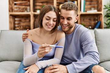 Young caucasian couple smiling happy looking pregnant test result at home.