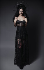 Halloween theme: beautiful young witch in black dress and headwear with roses and spikes. Dark...