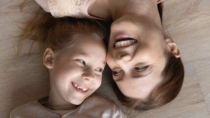 Close up top view of smiling little teen girl child and young Caucasian mother lying on floor play together at home. Happy mom and small daughter have fun relax on family weekend. Laughter concept.