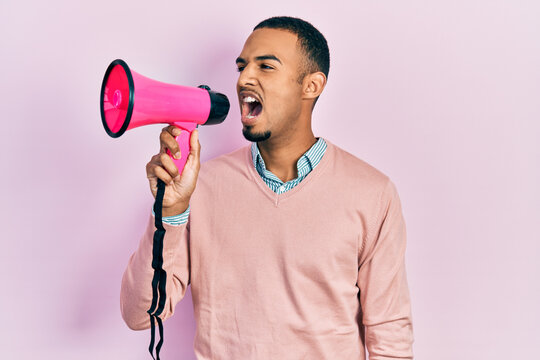 Young african american man shouthing and screaming through megaphone over pink isolated background