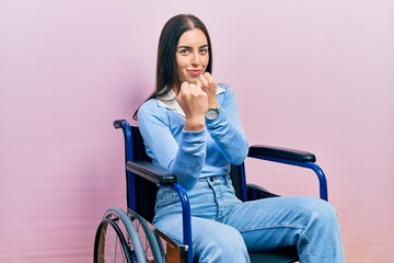 Beautiful woman with blue eyes sitting on wheelchair ready to fight with fist defense gesture,...