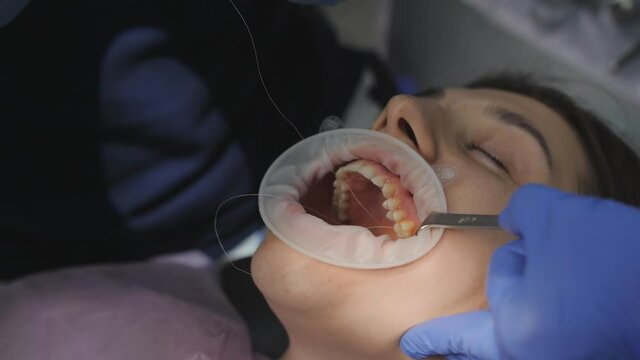 Face of patient, hands of dentist sutured wound after tooth extraction and assistant