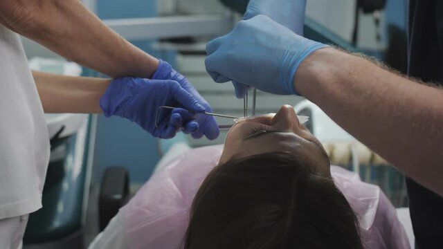 Face of patient, hands of dentist sutured wound after tooth extraction and assistant