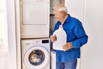 Senior caucasian man smiling happy holding detergent standing by washing machine at the terrace.