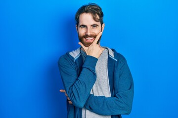 Caucasian man with beard wearing casual sweatshirt looking confident at the camera smiling with crossed arms and hand raised on chin. thinking positive.
