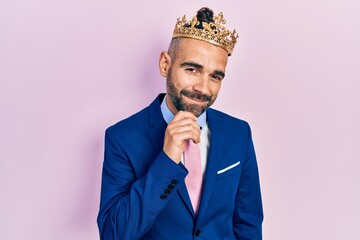 Young hispanic man wearing business clothes and king crown smiling looking confident at the camera...