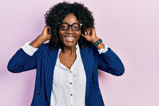 Young african american woman wearing business clothes and glasses smiling pulling ears with fingers, funny gesture. audition problem