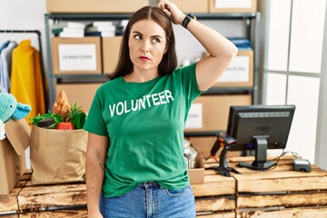 Young brunette woman wearing volunteer t shirt at donations stand confuse and wondering about...