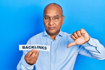 Middle age latin man holding paper with backlinks message with angry face, negative sign showing...