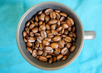 a dark gray mug with whole coffee beans stands on a blue background . top view