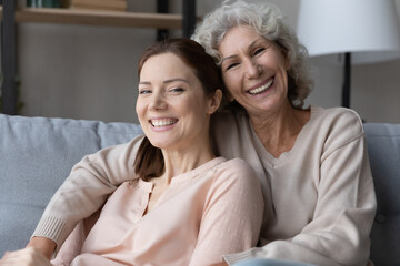 Portrait of happy old Caucasian mother and adult daughter rest on sofa at home hug cuddle together. Smiling mature mom and grownup woman child relax on couch show love and care in family relations.