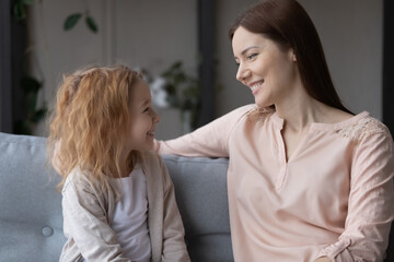 Smiling loving young Caucasian mother relax on couch with teen little daughter chat and talk. Happy caring mom rest on sofa with small teenage girl child, enjoy good leisure family weekend together.