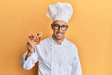 Bald man with beard wearing professional cook apron holding italian pizza looking positive and happy standing and smiling with a confident smile showing teeth