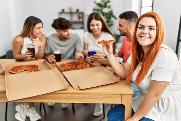 Fototapeta na wymiar Group of young people smiling happy eating italian pizza sitting on the table at home