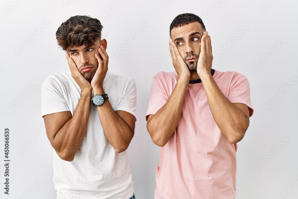 Wall mural young gay couple standing over isolated background tired hands covering face, depression and sadness