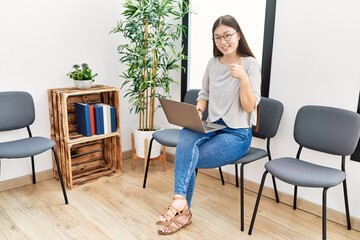 Fototapeta premium Young asian nurse woman sitting at waiting room using laptop smiling happy and positive, thumb up doing excellent and approval sign