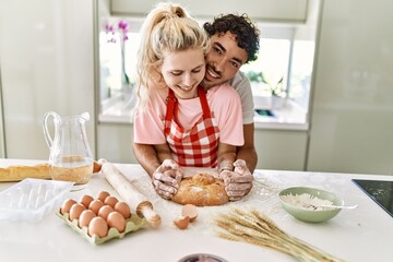 Young couple smiling happy cooking homemade bread at kitchen.