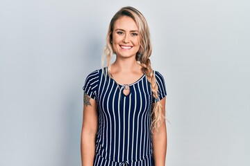 Beautiful young blonde woman wearing casual striped dress with a happy and cool smile on face. lucky person.