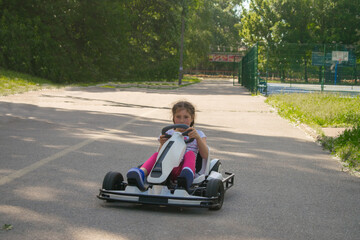 A child rides an electric go-kart in a city park. A young girl learns to drive an electric car. - obrazy, fototapety, plakaty