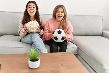 Young couple watching soccer match eating porpcorn at home.