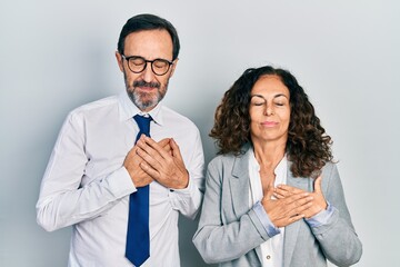 Middle age couple of hispanic woman and man wearing business office uniform smiling with hands on chest with closed eyes and grateful gesture on face. health concept.