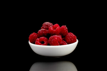 Several berries of ripe red raspberries on a white ceramic saucer, close-up, isolated on black.