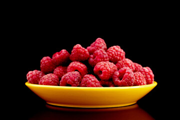 Several berries of ripe red raspberries on a yellow ceramic saucer, close-up, isolated on black.