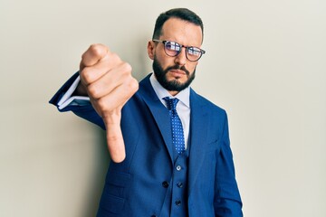 Young man with beard wearing business suit and tie looking unhappy and angry showing rejection and negative with thumbs down gesture. bad expression.