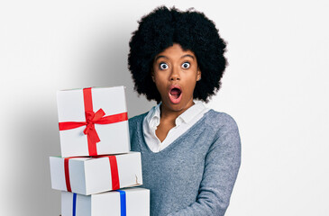 Young african american woman holding gifts afraid and shocked with surprise and amazed expression, fear and excited face.