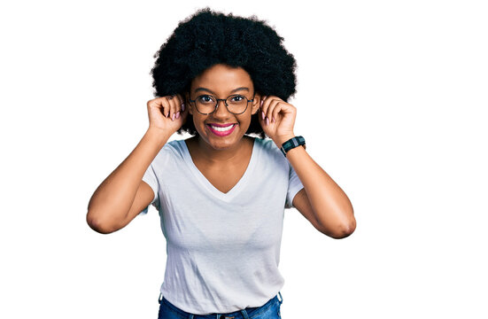 Young african american woman wearing casual white t shirt smiling pulling ears with fingers, funny gesture. audition problem