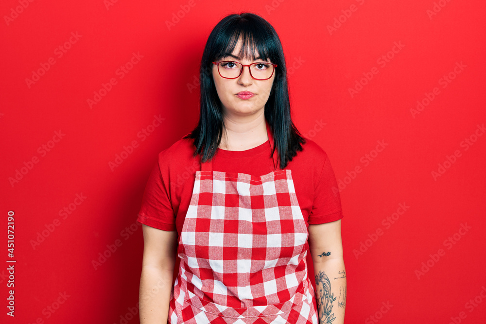 Sticker Young hispanic woman wearing cook apron and glasses relaxed with serious expression on face. simple and natural looking at the camera.