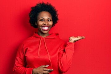 Young african american woman wearing casual sweatshirt smiling cheerful presenting and pointing with palm of hand looking at the camera.