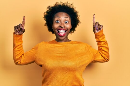 Young african american woman wearing casual clothes smiling amazed and surprised and pointing up with fingers and raised arms.
