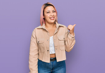 Hispanic woman with pink hair wearing casual clothes smiling with happy face looking and pointing to the side with thumb up.